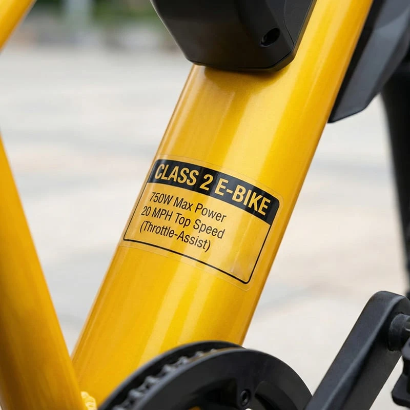 A standard US E-Bike Class 2 label sticker on a bike frame, clearly displaying 750W motor limit and 20mph top speed for street legal compliance.