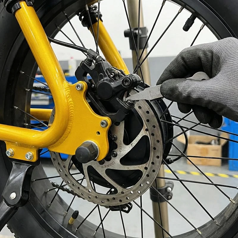 Close-up view of a mechanic checking the hydraulic disc brake pads on an F6 e-bike, ensuring the pad material is thicker than 1mm for safe braking.